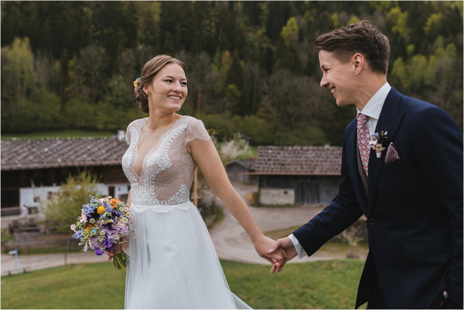 Brautpaar lacht sich an und läuft über eine Wiese