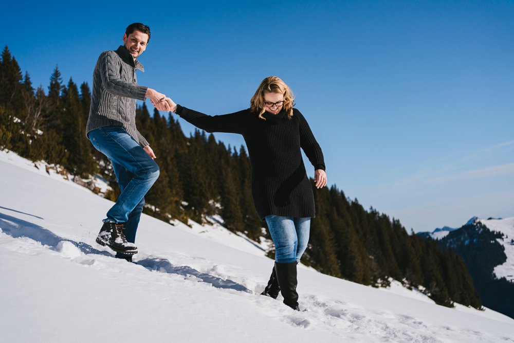 Pärchen läuft einen Hang im Schnee runter bei ihren Verlobungsfotos